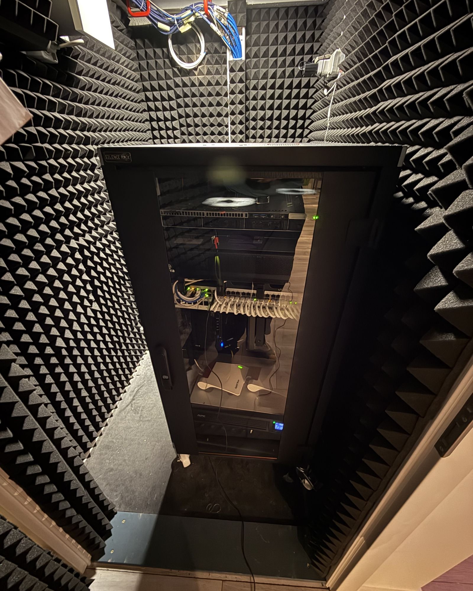Kleiner Technikraum mit Schallschutz-Schaumstoff an den Wänden und einem Netzwerkschrank mit Glastür