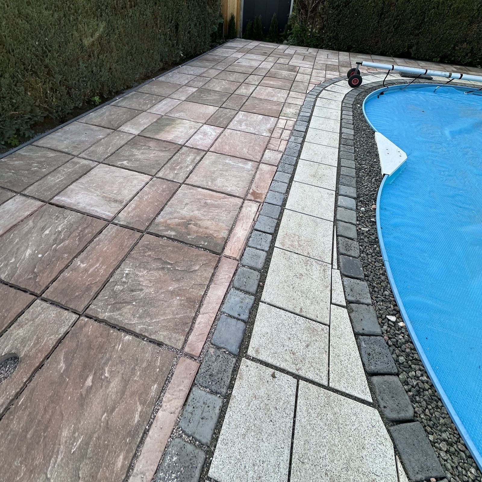 Terrasse aus großen Natursteinplatten neben einem Pool, eingerahmt von dichten Hecken